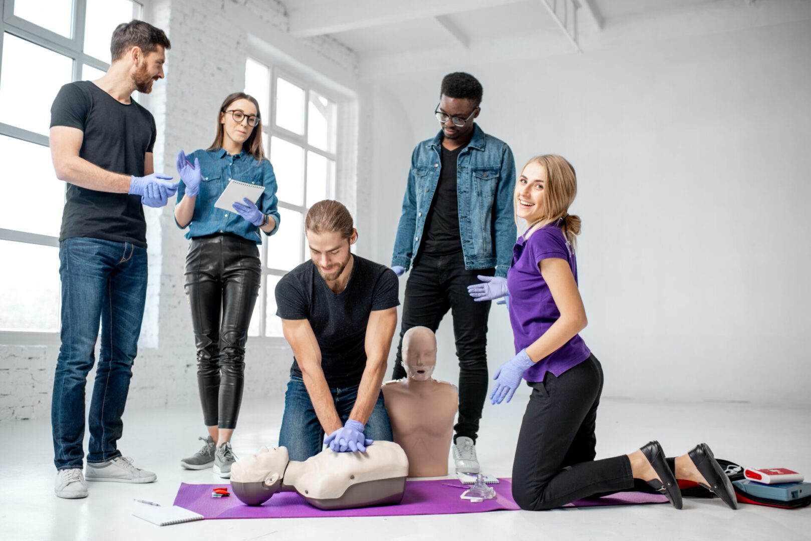Group of young people practising to make artificial breathing with instructor and medical dummies during the first aid training indoors