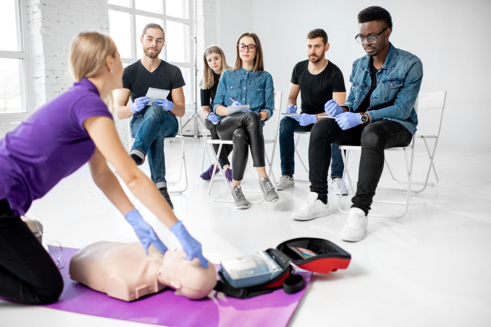 Group of young people sitting and listening to the instructor showing some practise with medic dummy during the first aid training indoors