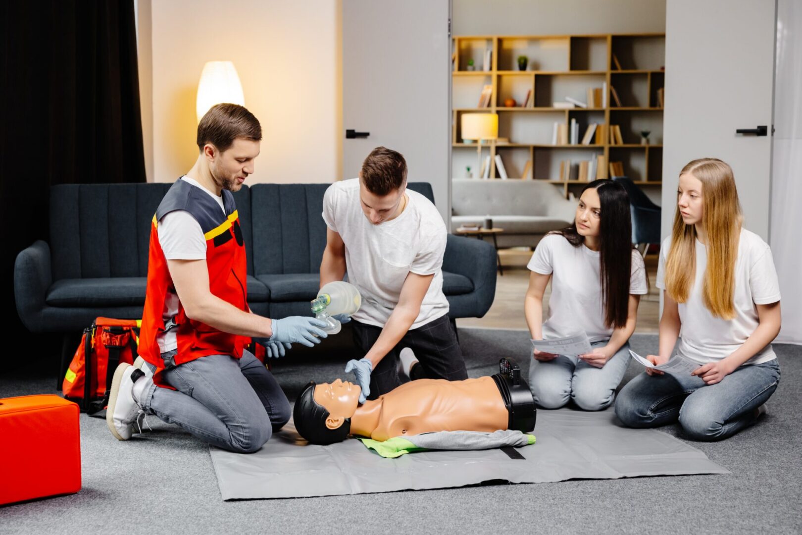 Young man instructor helping to make first aid heart compressions with dummy during the group training indoors.